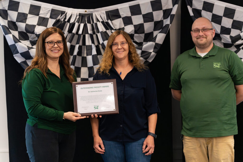 Three people on stage holding an award certificate at S&T’s Staff Appreciation Day event.