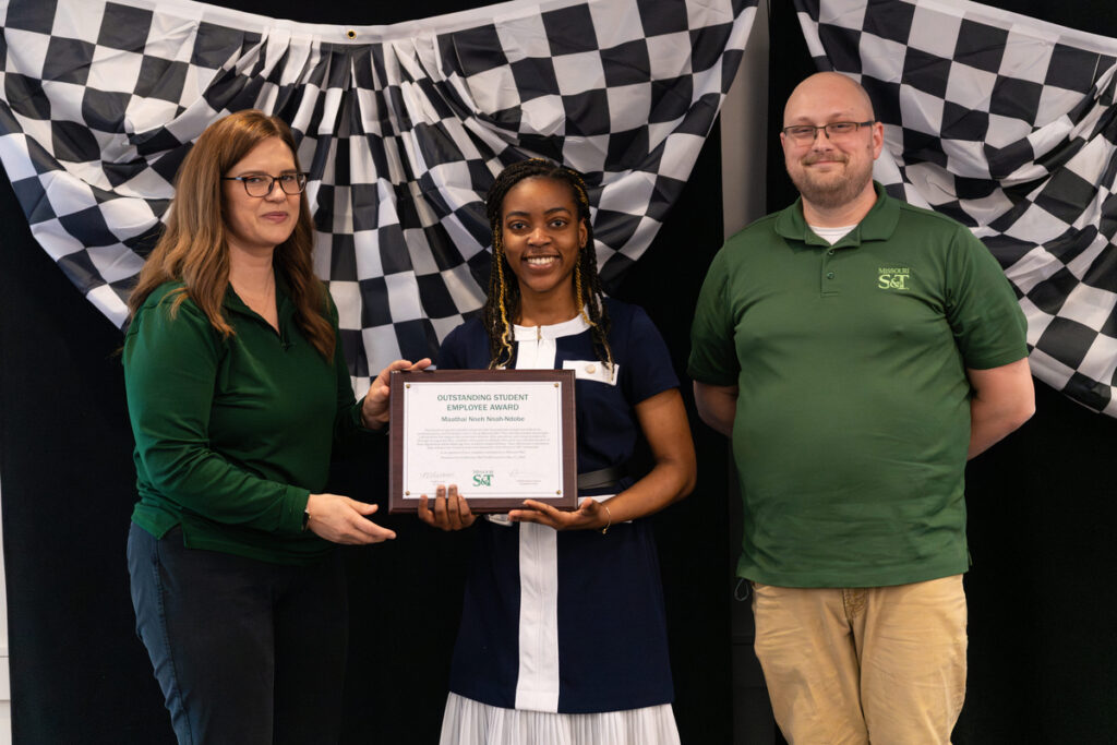 Three people pose on stage holding an “Outstanding Student Employee Award” certificate at a Missouri S&T event.