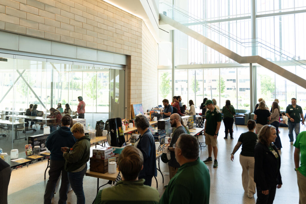 People browsing raffle prizes and chatting around tables in a bright lobby space during S&T’s Staff Appreciation Day event.