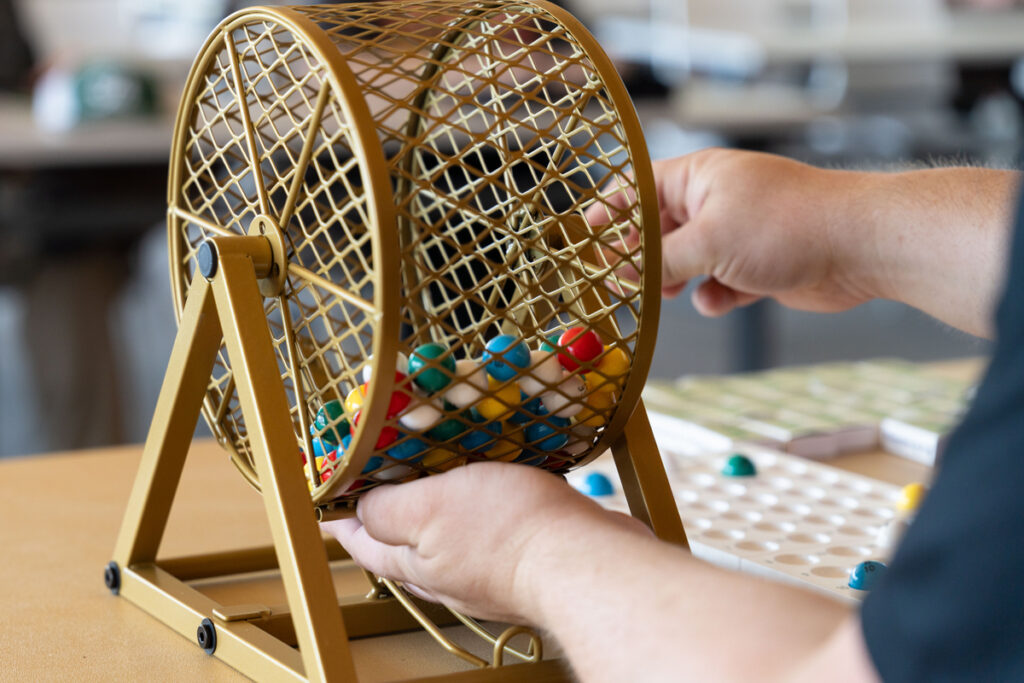 Close-up of hands turning a gold bingo-style cage filled with colorful numbered balls.