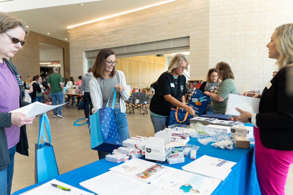 People browsing items on tables in a bright lobby during S&T’s Staff Appreciation Day event.