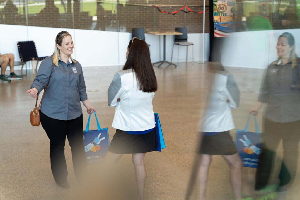 Two people talking in a lobby while holding event swag bags at S&T’s Staff Appreciation Day event.