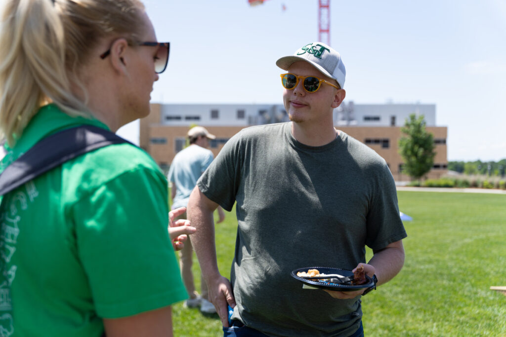 Two people talking outdoors on a grassy lawn while one holds a plate of food at S&T’s Staff Appreciation Day event.