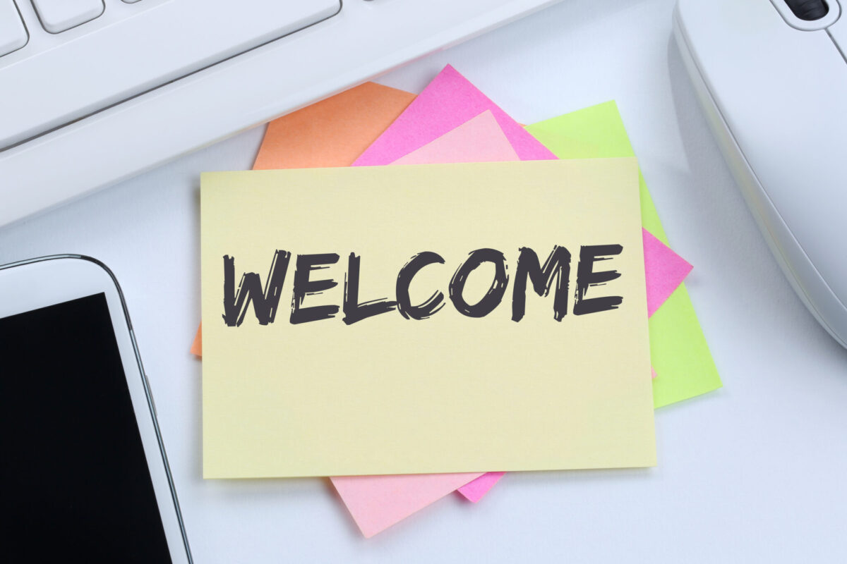 A stack of post-its on a desk next to a cell phone and keyboard that says "Welcome."