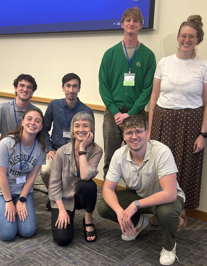 A group of seven people pose for a photo, some kneeling and some standing.