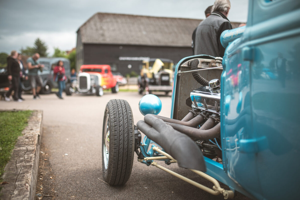 Turquoise hot rod with exposed engine at a car show.