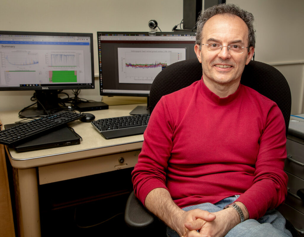 Man in red shirt sitting in front of two computer monitors.