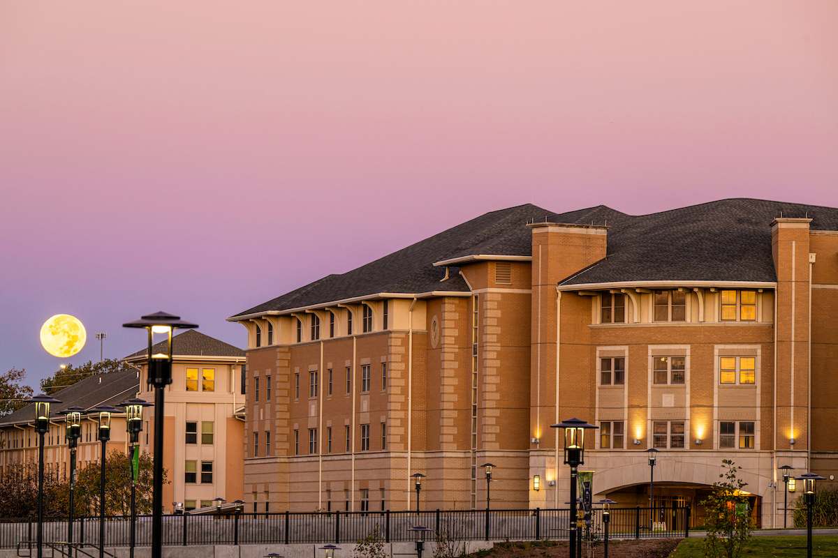 The Residential Commons 1 building with a full moon in the sky behind it.