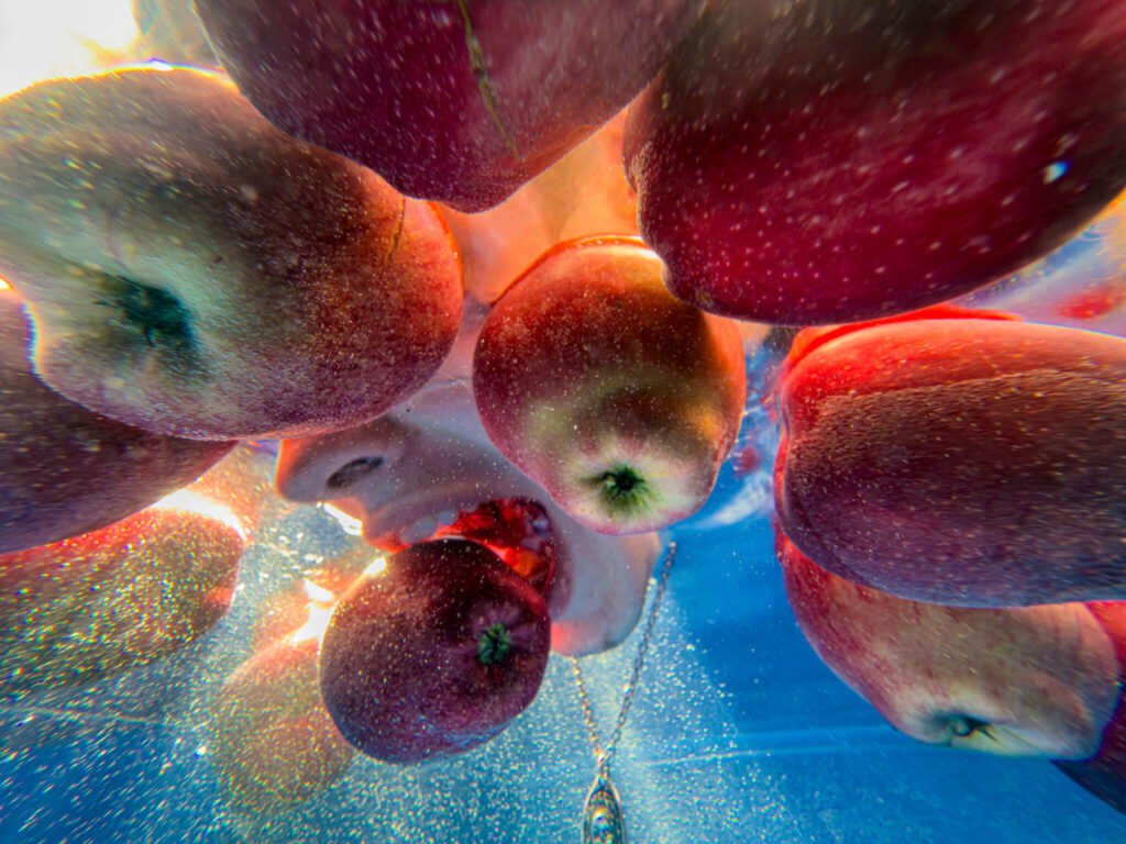 Underwater view of apples floating around a person biting into an apple, with sunlight filtering through the water.