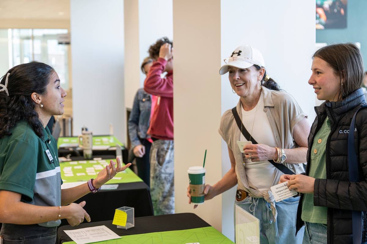 Individuals talk with a representative at an information table during a campus event.