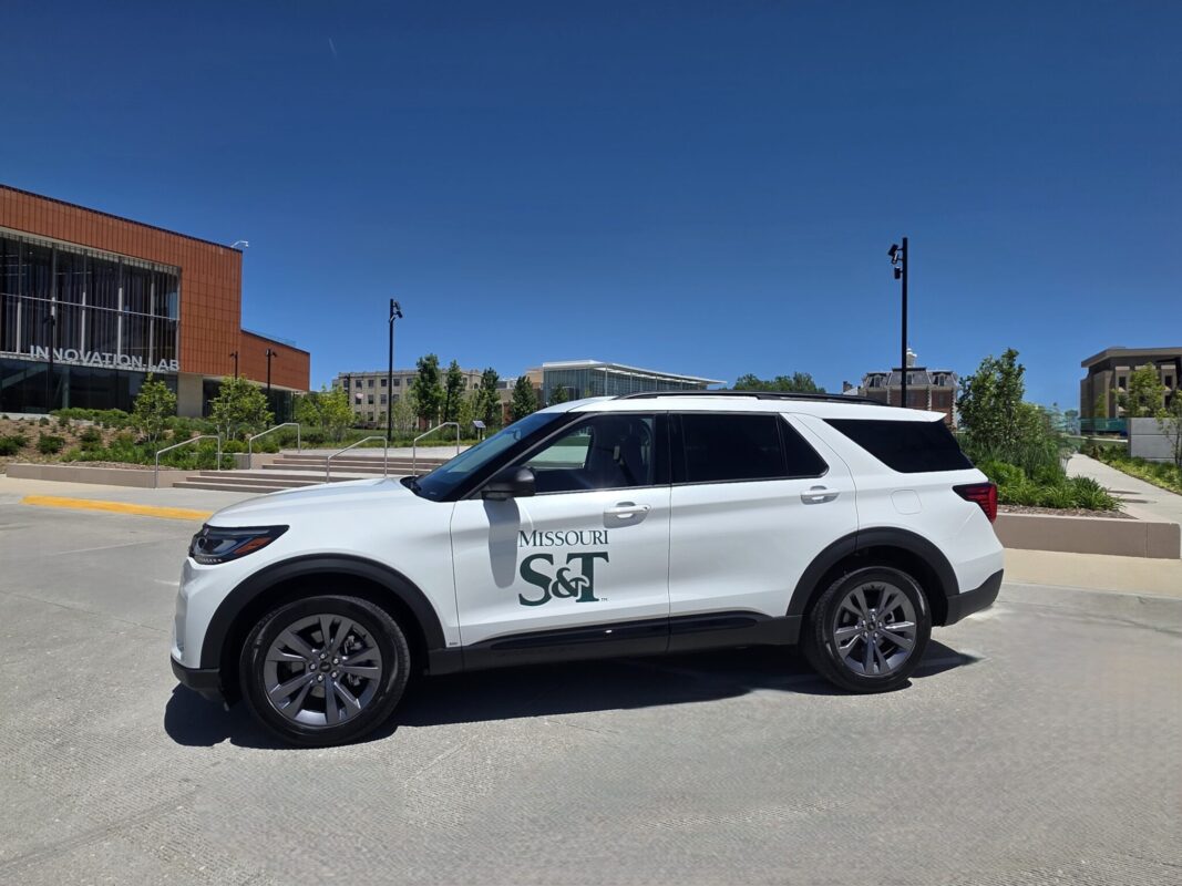White Missouri S&T vehicle parked on a campus roadway with academic buildings in the background.