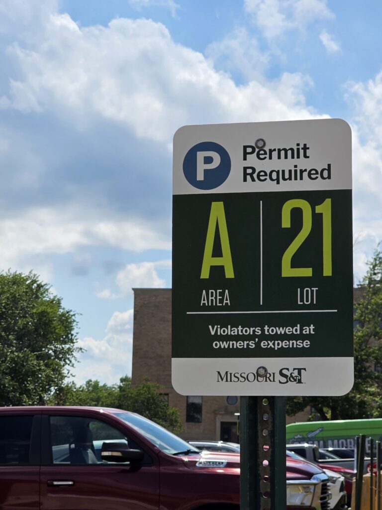 A sign for a parking lot designated as area A lot 21 informing that a permit is required and that violators will be towed at the owners' expense. 