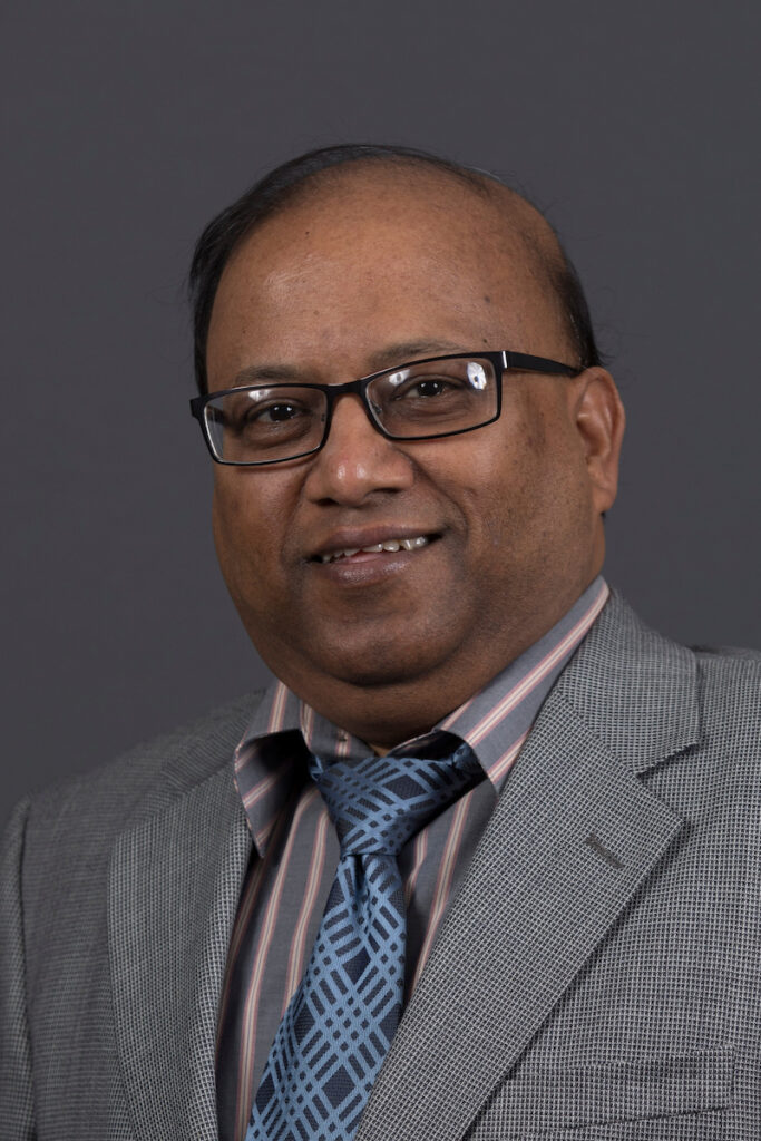 Professional headshot of Dr. Sanjay Madria wearing rectangular glasses, a gray textured suit jacket, a striped dress shirt and patterned blue tie.