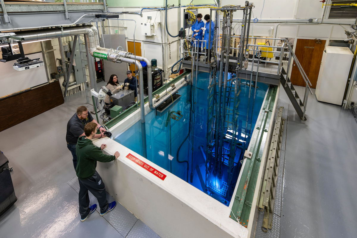 Missouri S&T Nuclear Reactor pool with clear blue water, reactor equipment, and visitors observing the facility from the pool edge and an elevated platform.