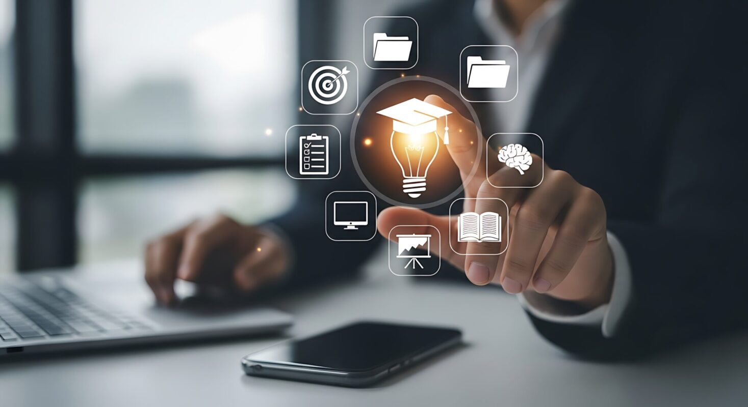 Person working on a laptop points to a glowing lightbulb icon surrounded by digital education and learning symbols, including a graduation cap, books, folders and a presentation screen.