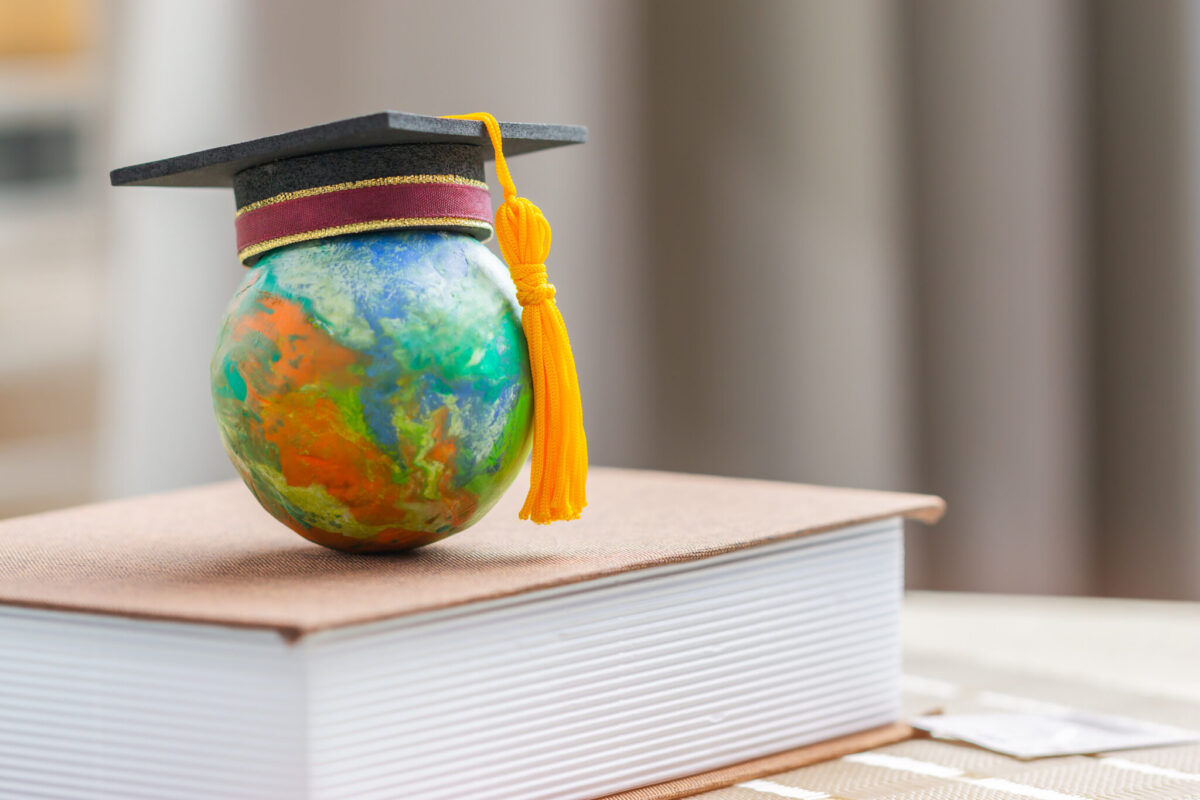 Small globe painted with a world map and topped with a graduation cap rests on a closed book.