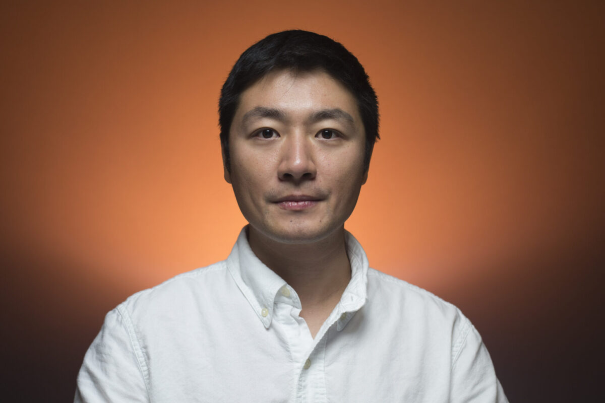 Headshot of a person in a white button-down shirt against an orange gradient background.