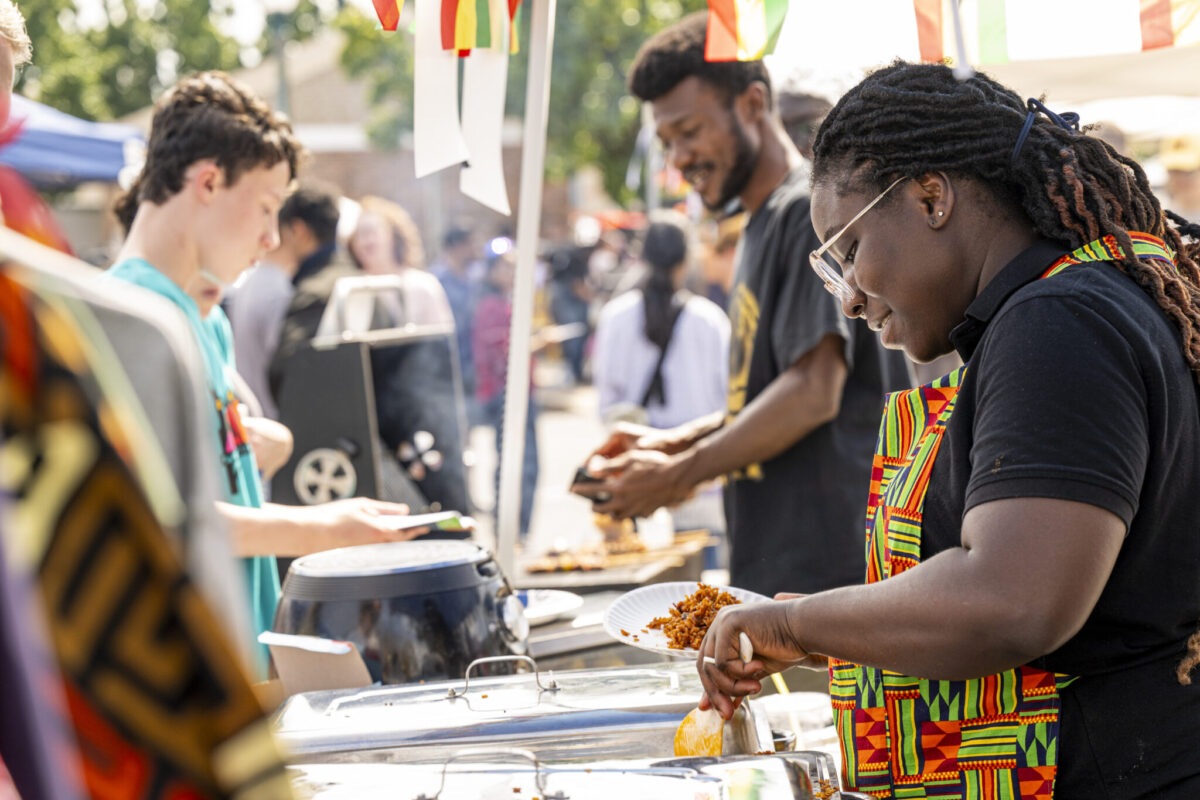 A vendor in a colorful patterned apron serves food to attendees at Celebration of Nations.