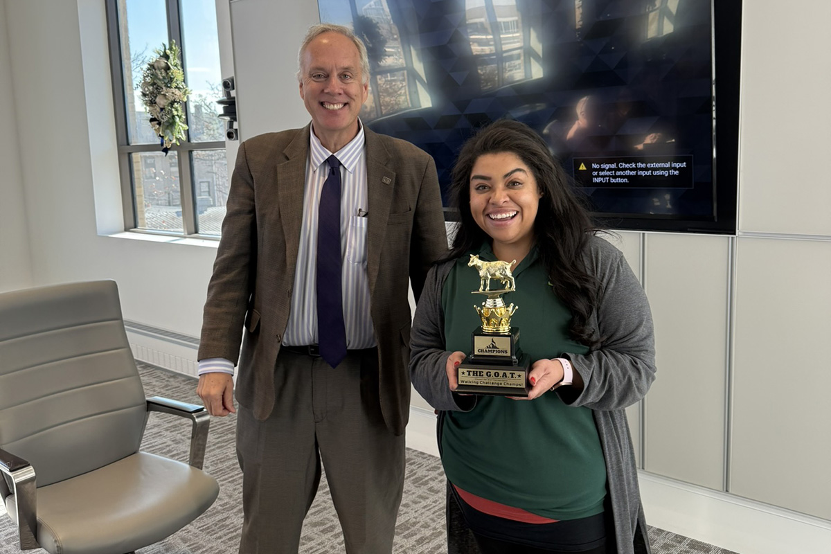 Two individuals pose with a trophy in a conference room.