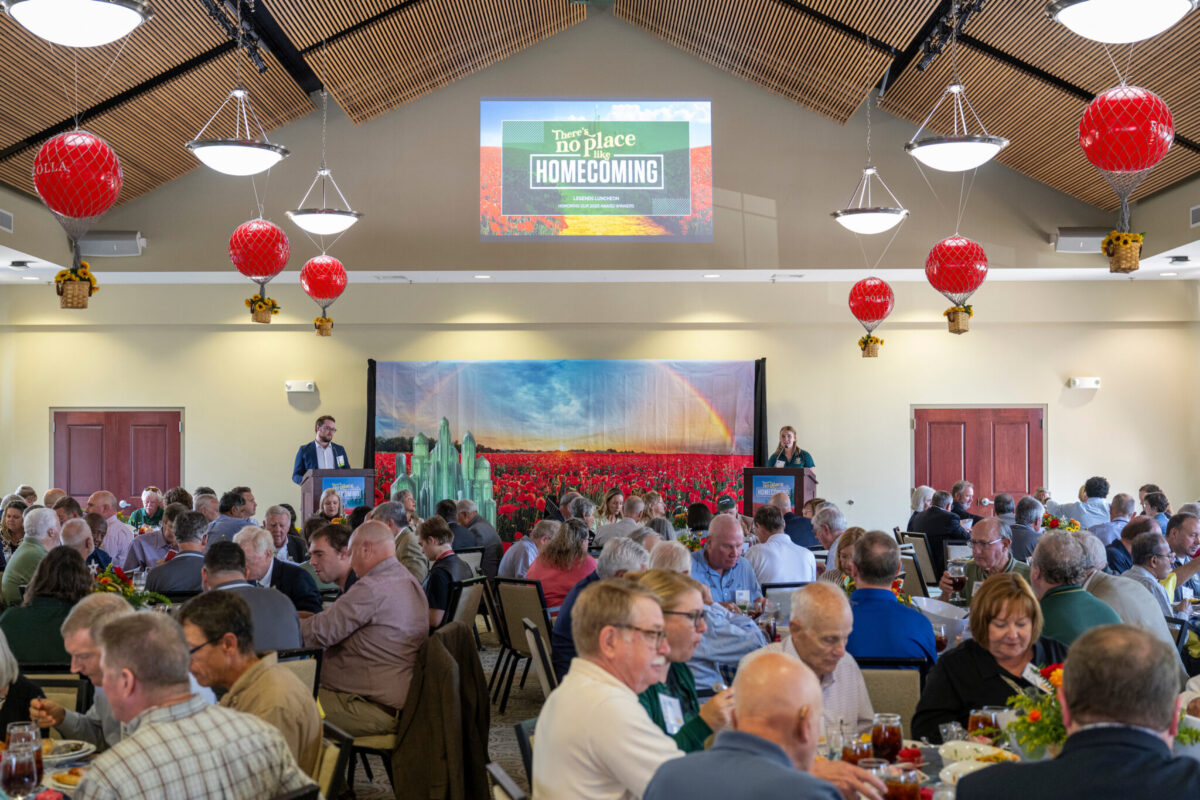 A large crowd seated at dining tables during a cultural event in a banquet hall decorated with red lanterns.