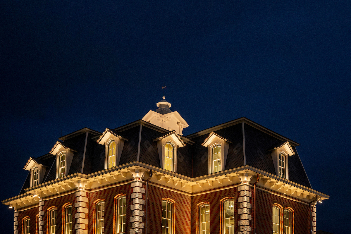 A brick building with illuminated windows and a dark roof stands against a deep blue night sky.