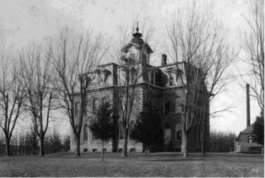 Black-and-white photograph of a historic multi-story brick building with an ornate roofline and cupola, surrounded by leafless trees.
